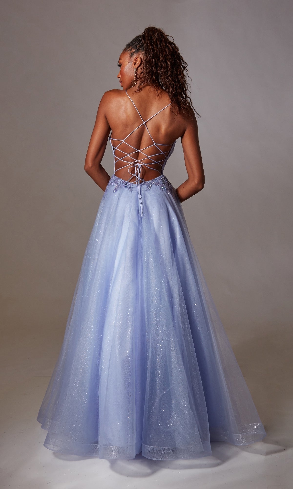 A woman stands facing away against a neutral background in the Aerie Couture 265 Deep V-Neck Long Prom Ball Gown, featuring a floor-length light purple a-line silhouette with an embroidered lace-up open back.